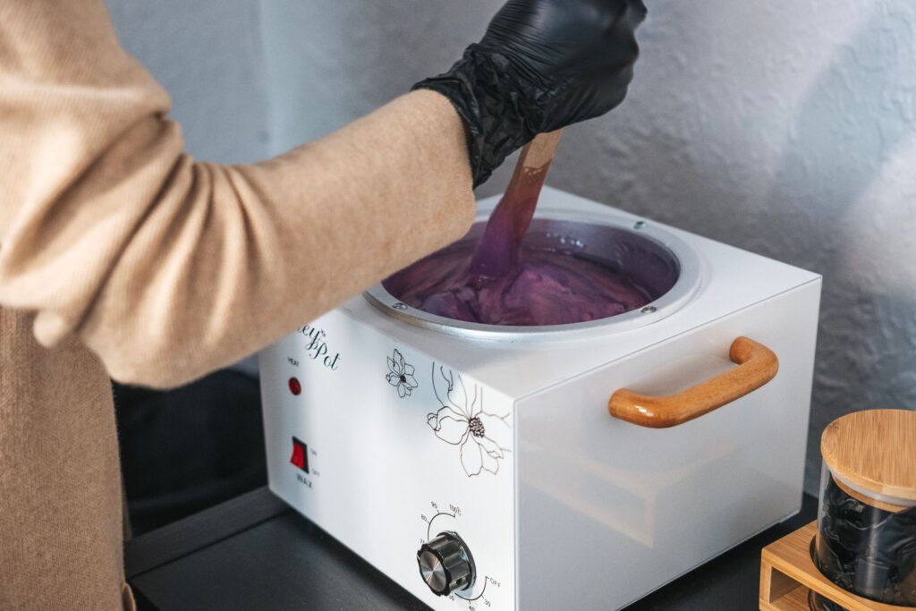 Therapist stirring warm hot wax in a wax heater