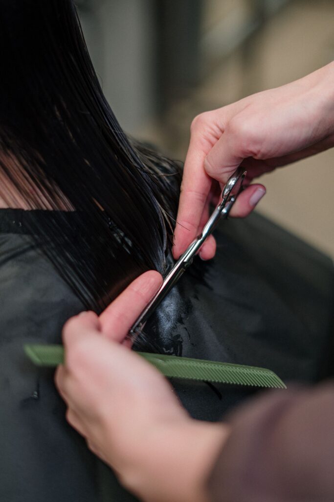 Hairdresser cutting a client's long dark hair with scissors
